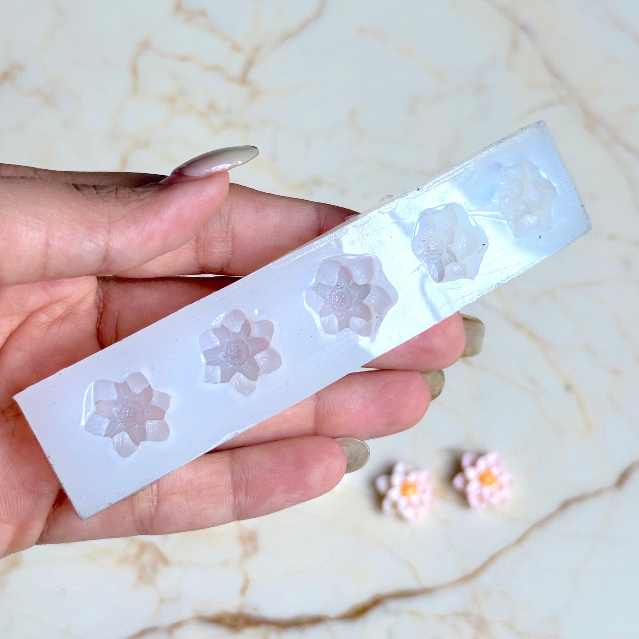 Hand holding a silicone mold with flower shapes on a marble surface